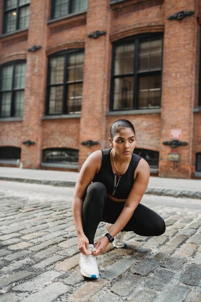 Confident woman ties shoelaces, ready for an urban jog, embodying vitality and fitness.