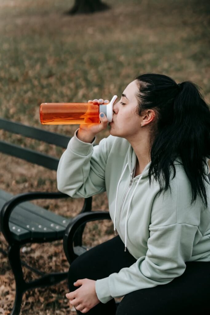A young woman in a hoodie hydrating on a park bench during her workout break.