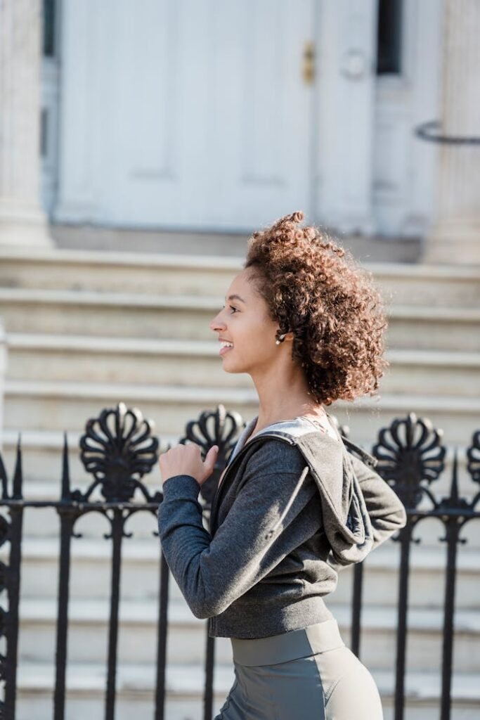 Side view of black female in activewear running along iron fence on blurred background